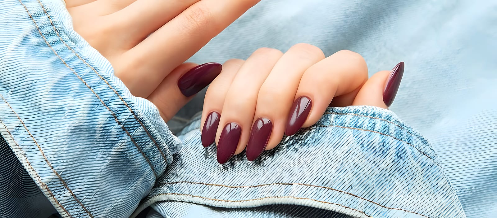 Manicured dark red nails against a denim sleeve